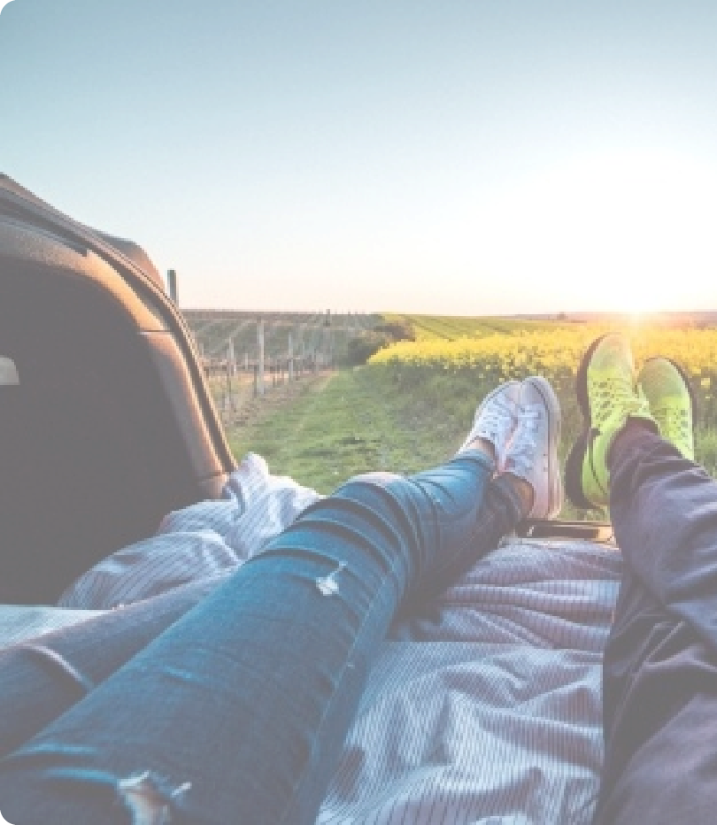 two sets of legs on laying on a blanket looking at a field with setting sun